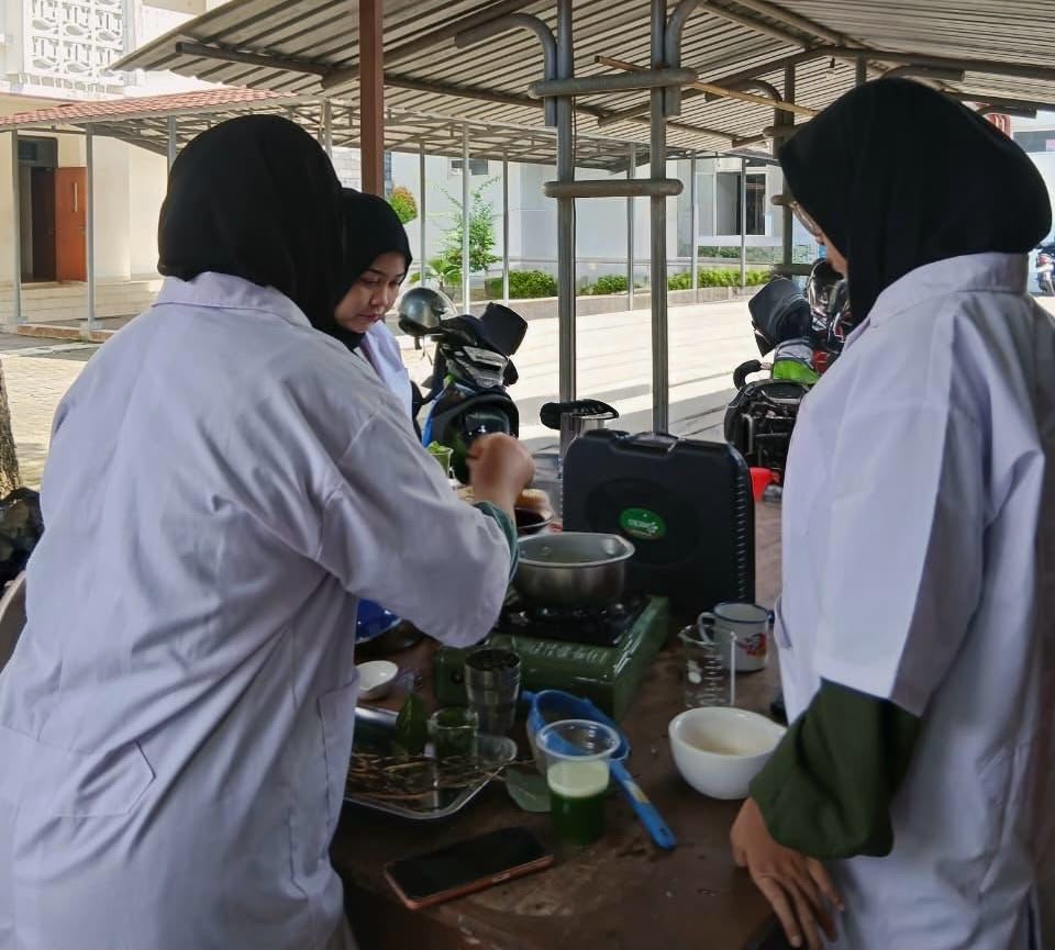 Whatsapp image 20260617 at 20 58 48 catrawarta Three women in hijabs and white lab coats cook at a portable stove on a table outdoors with bowls and cups nearby under a covered area